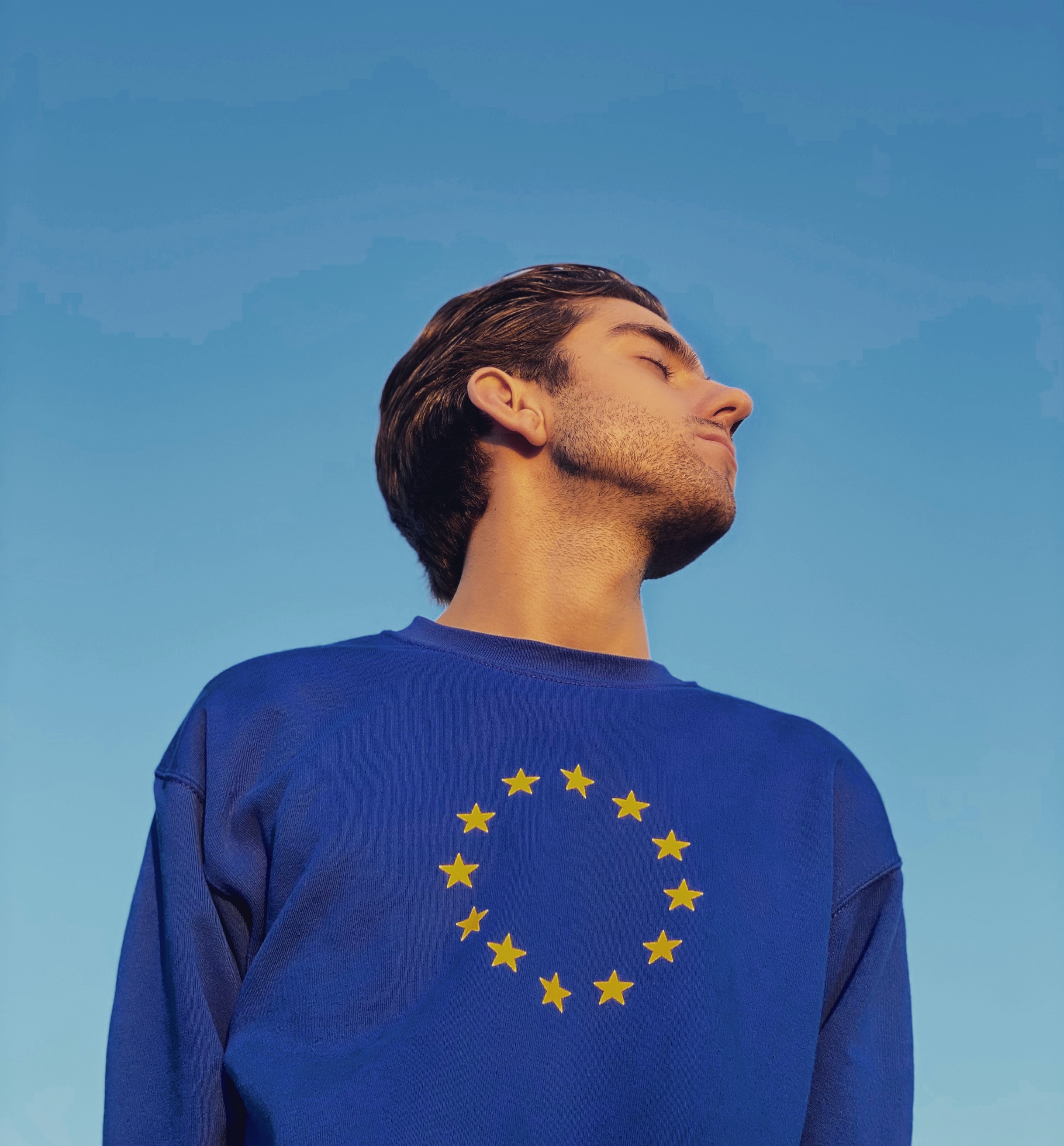muž s modrým svetrem a vlajkou Evropské unie