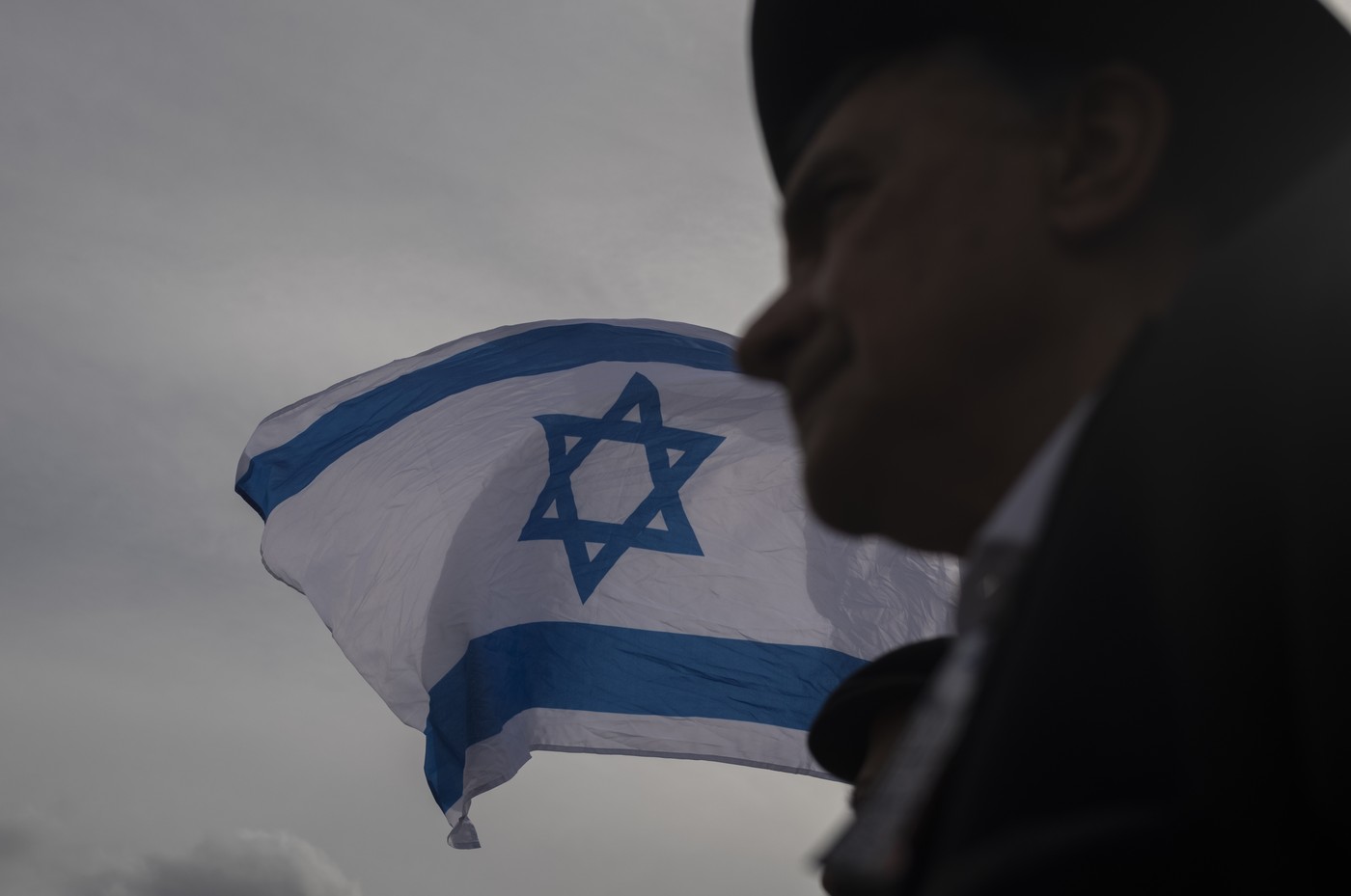 Muž stojící před vlajkou Izraele.